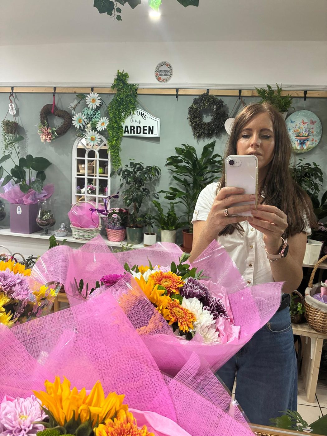 Jolie inside the shop with bouquets wrapped in pink, wreaths and plants along the back wall