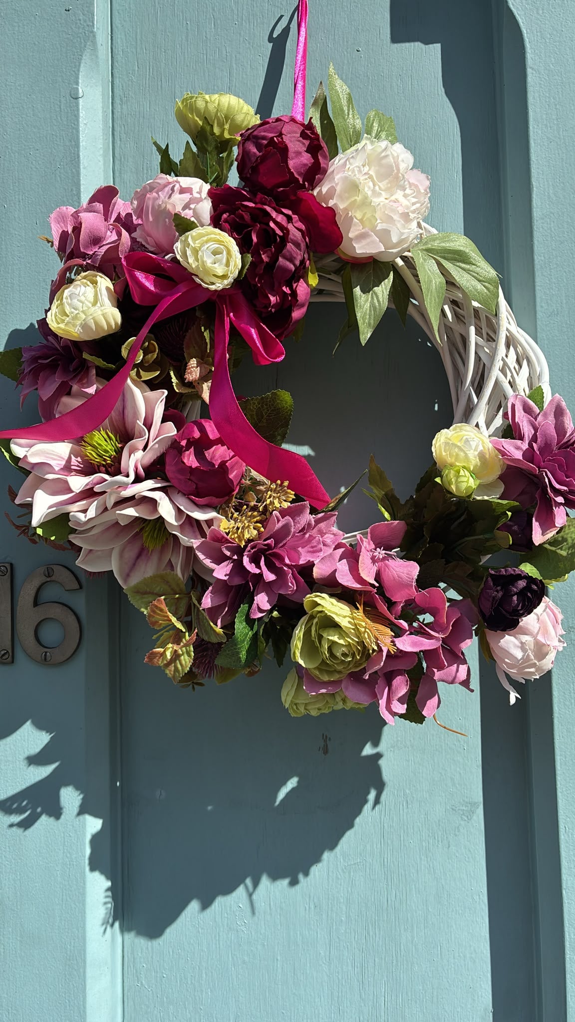 Magnolia and peony wreath hanging on a blue front door