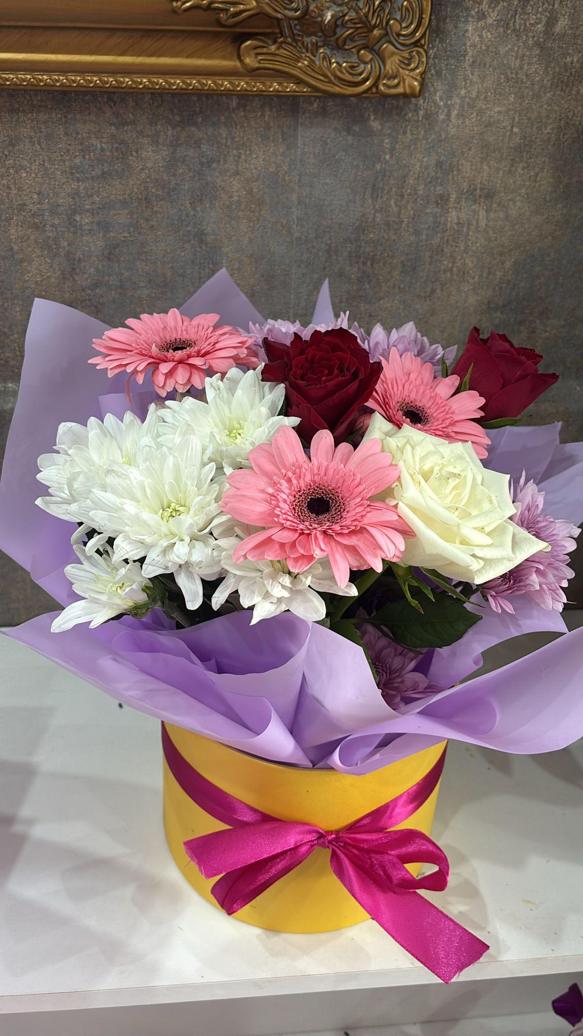 Medium bouquet of pink gerbera, white chrysanthemum and roses in a yellow hat box with a pink ribbon